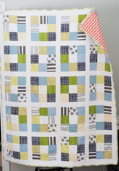 a baby quilt hanging from the side of a white crib with green, blue and yellow squares on it