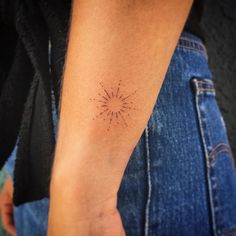 a person's arm with a small sunburst tattoo on the left forearm