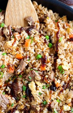 a skillet filled with rice, meat and veggies next to a wooden spoon