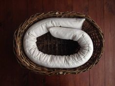 a wicker basket with two pillows in it sitting on a wooden floor next to a wall