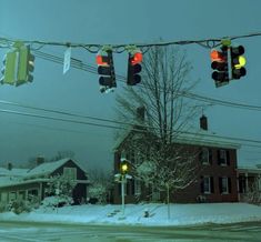 traffic lights are hanging over the snow covered street in front of houses and power lines