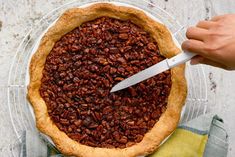 a person cutting into a pecan pie on top of a glass plate with a knife