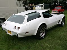 a white sports car parked on top of a lush green field next to other cars