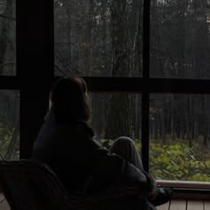 a person sitting in a chair looking out a window at the woods outside and trees