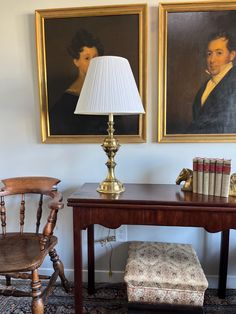 two paintings hang on the wall next to a desk with a lamp and chair in front of it