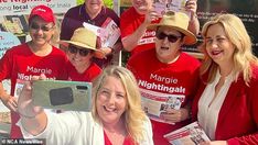 a group of people in red shirts and hats holding up cell phones while standing next to each other