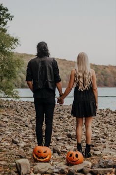 a man and woman holding hands while walking on rocks with pumpkins