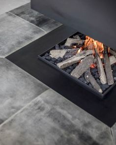 an outdoor fire pit with rocks and logs in the center, surrounded by grey tiles