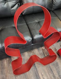 a red sculpture sitting on top of a wooden floor next to a black leather couch