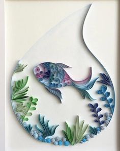 a paper cut fish with blue and green leaves on it's side, in a white frame