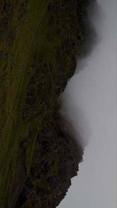 an airplane is flying over the top of a cliff on a foggy day in the mountains