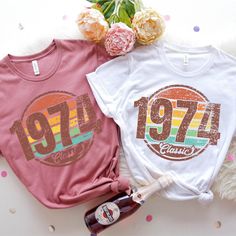 two t - shirts with the year 1971 and 1974 printed on them next to a bottle of wine