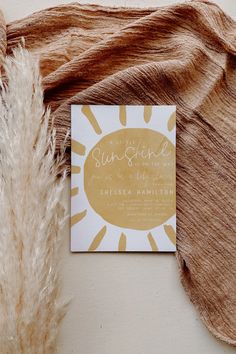 a yellow and white business card sitting on top of a brown blanket next to a feather