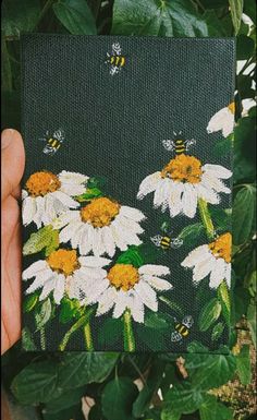 a hand holding up a piece of fabric with white and yellow daisies on it