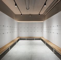 an empty room with white lockers and wooden benches in front of the wall,