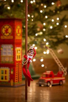 an elf is hanging on the pole next to a toy firetruck and christmas tree