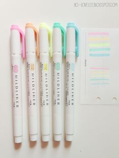 four pens lined up next to each other on top of a white surface with colorful writing