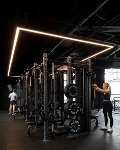 a woman standing in front of a gym machine with lights on the ceiling above her