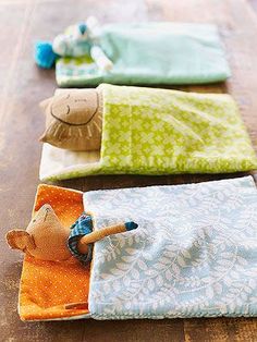 three small stuffed animals sitting on top of folded cloths in the middle of a wooden floor