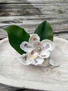 a small white flower sitting on top of a wooden tray next to a green leaf