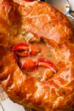 a lobster pot pie on a plate with sauce in the middle and two spoons to the side