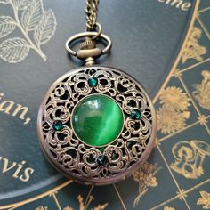 "This unique old fashioned styled pocket watch features a green cabochon at the center surrounded by emerald colored Swarovski crystals.  The clock face is revealed by pushing a button at the top.   There is also a mechanism, located at the top, that you can use to adjust the time.    A battery IS included in the watch so there is no need to purchase one separately.   The pocket watch measures  2-1/2\" tall and 2\" wide and it will come on a bronze chain in the length of your choice. Tip: If you Fancy Pocket Watch, Fantasy Watch, Pocket Clock, Pocket Watch Art, Steampunk Pocket Watch, Old Pocket Watches, Antique Pocket Watch, Steampunk Watch, Pocket Watch Necklace