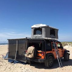 an orange jeep parked on top of a sandy beach next to the ocean with a tent