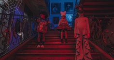 two children in costumes walking down the stairs with red light on them and one child wearing cat ears