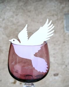 a wine glass with a white bird on the top and pink bottom, sitting in front of a stone wall