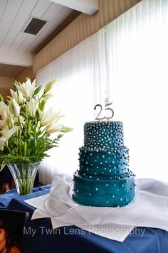 a blue wedding cake sitting on top of a table next to a vase filled with flowers