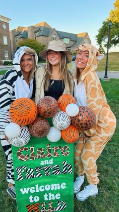 three women dressed in animal costumes holding a welcome to the zoo sign with balloons on it