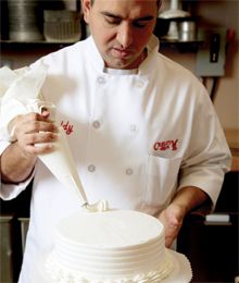 a man in a chef's uniform cutting into a white cake