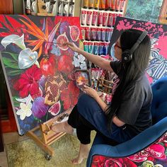 a woman sitting in front of a painting with headphones on and her hands holding the paint brush