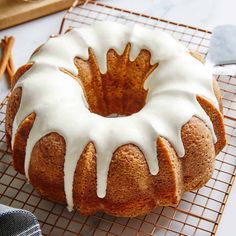 a bundt cake with white icing on a cooling rack next to cinnamon sticks