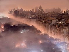 an aerial view of a city at night with fog in the air and lights on buildings