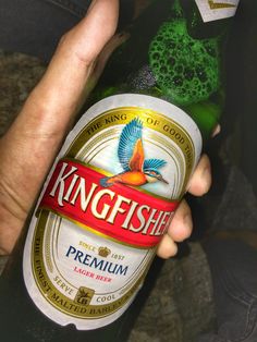 a person holding a bottle of beer in their hand with a green bird on it