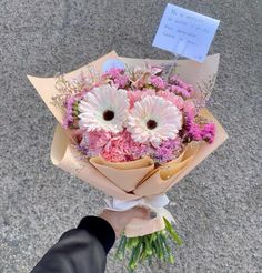 a person holding a bouquet of flowers in their hand with a note attached to it