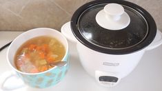 a bowl of soup next to an electric pressure cooker on a white counter top