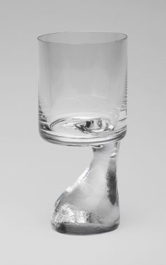 an empty glass sitting on top of a white table next to a silver object in the shape of a foot