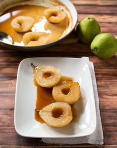 some apples are sitting on a plate with caramel sauce in the middle and two pears next to it