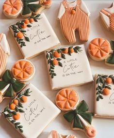 cookies decorated with oranges and baby ones are arranged on a white tablecloth that says, little one is on the way