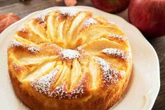 a white plate topped with a pastry covered in powdered sugar next to an apple