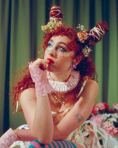 a woman with red hair and makeup sitting on a bed