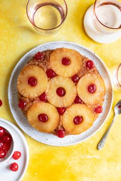 a pineapple upside down cake on a plate with cherries next to it and glasses of water