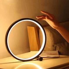 a person holding their hand up to a round mirror on a table next to a book