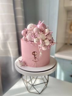 a pink and white cake with balloons on top is sitting on a stand in front of a window