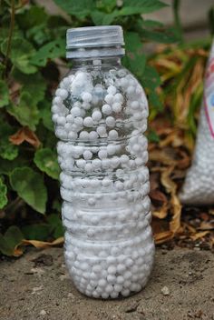 a bottle filled with white balls sitting on the ground next to some plants and dirt