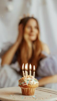 a cupcake with lit candles sitting on a table in front of a woman's face