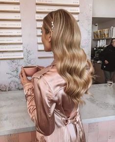 a woman with long blonde hair is holding a cup and looking at the wall behind her