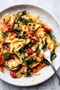 a white plate topped with pasta covered in sauce and garnished with fresh herbs